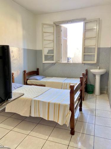 two beds in a room with a tv and a sink at Hotel Avenida Bauru in Bauru