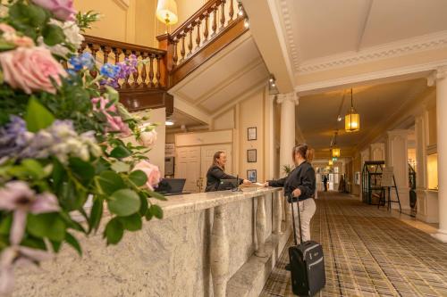 a woman with a suitcase standing at a counter in a building at Peebles Hydro in Peebles