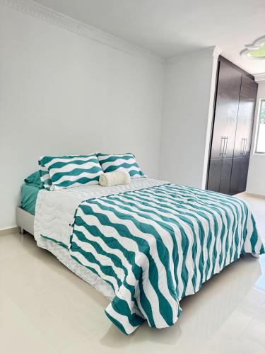 a white bedroom with a bed with a blue and white striped blanket at Casa Encanto Para Grupos y Familias in Bucaramanga