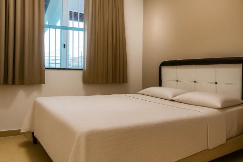 a bedroom with a large white bed with a window at Apartamento charmoso 3/4 in Ilhéus