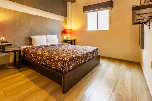 a bedroom with a bed and a desk and a window at Capital O Hotel Del Parque Guadalajara in Guadalajara