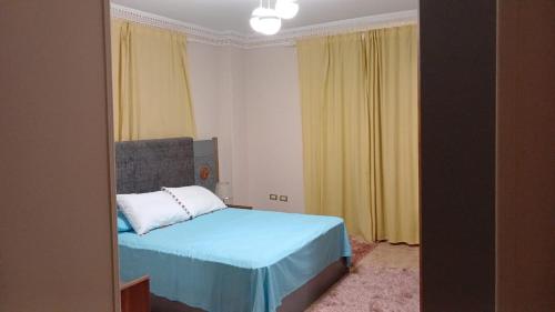 a bedroom with a blue bed and yellow curtains at Fully Brand New Furnished Apartment in Sheikh Zayed