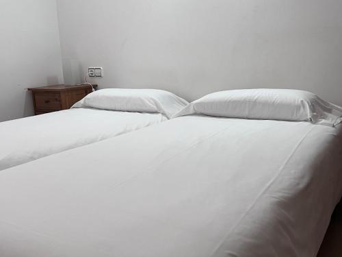 two beds in a room with white sheets and pillows at Cal Cisteller in Santa Pau