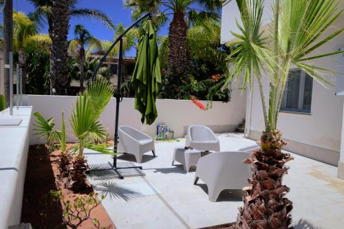 a patio with chairs and a umbrella and palm trees at Vacanze da Beppuccio Scoglitti in Vittoria