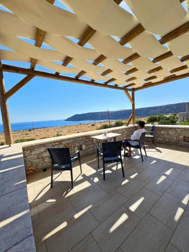 a man sitting at a table on a patio with a view of the beach at Armenopetra View Gerolimenas in Gerolimenas