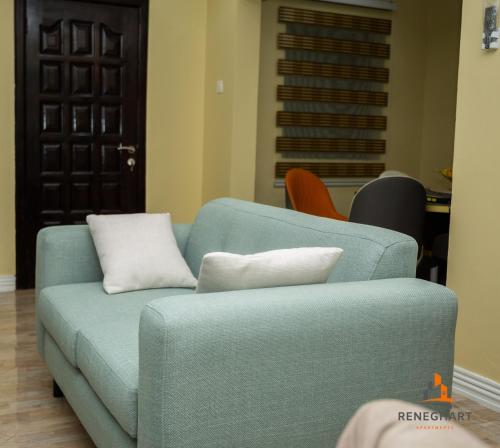 a blue couch with white pillows in a living room at ReneGhart Apartments in Kasoa