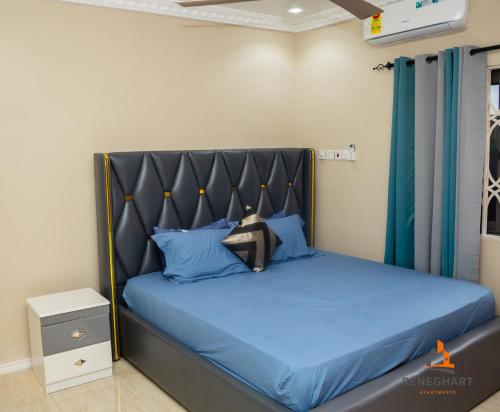 a bedroom with a blue bed with a black headboard at ReneGhart Apartments in Kasoa