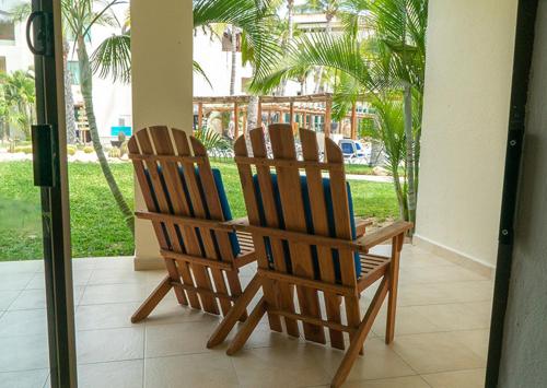 two wooden chairs sitting on a porch with palm trees at Grand Decameron Los Cabos, A Trademark All-Inclusive Resort in San José del Cabo