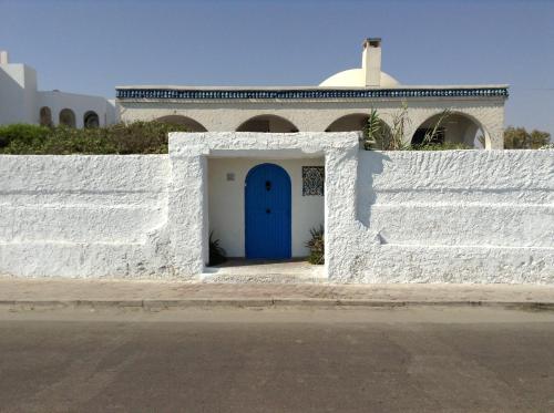 a white fence with a blue door in front of a building at La Brise de Djerba, Villa de Charme en bord de mer à Al Jazira in Mezraya