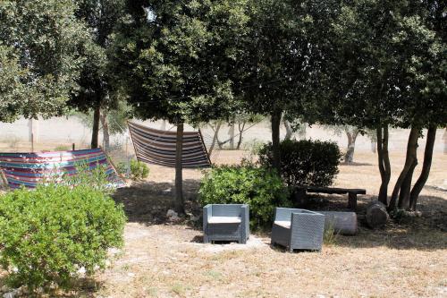 two chairs and a bench in a park with trees at Tenuta Petra Chiara in Torre Lapillo