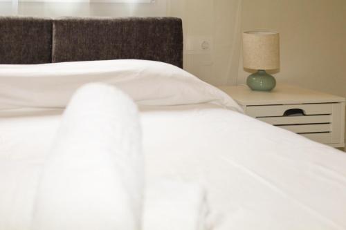 a bed with white sheets and a lamp on a night stand at ELAIA Αpartments in Alexandroupoli