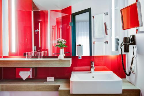 baño con paredes rojas y lavabo blanco en IntercityHotel Hamburg Altona en Hamburgo