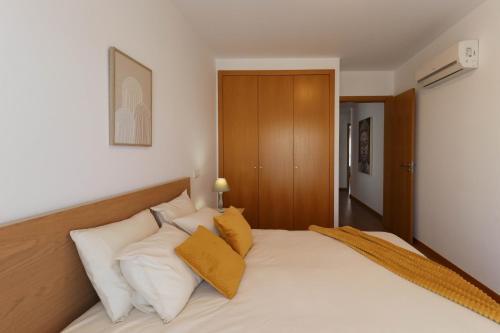 a bedroom with a bed with white sheets and yellow pillows at Apartamento Vista Marinha in Portimão