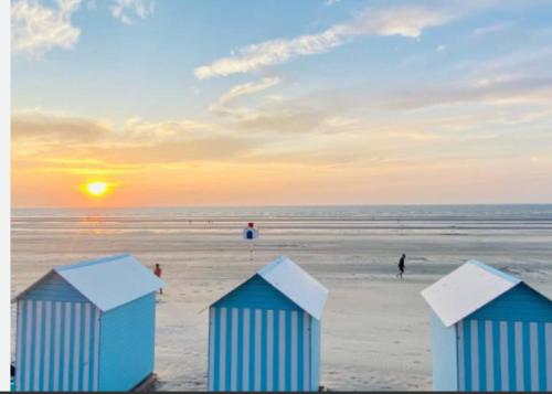 trois cabanes de plage bleues sur la plage au coucher du soleil dans l'établissement Appt RDC Jardin Laverie Parking Villa Margareth, à Dunkerque
