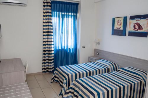 a room with two beds and a window with blue curtains at Holiday Affittacamere in Corigliano Calabro