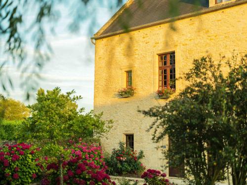 a brick building with flowers in front of it at Hôtel Le Manoir De Mathan Crépon à la campagne 5 mn d'Arromanches et 10 mn de Bayeux in Crépon