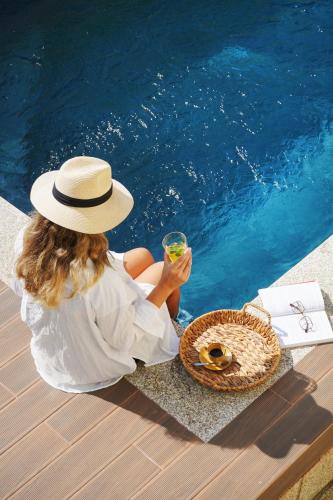a woman in a hat sitting next to a pool with a drink at Magníficos Dias Atlânticos in Moledo