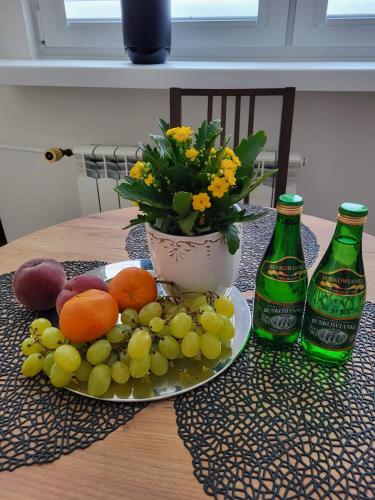 a plate of fruit and flowers on a table with two bottles at Apartament Max in Busko-Zdrój