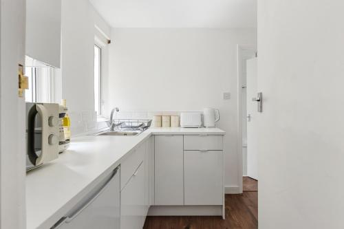a white kitchen with white cabinets and a sink at Modern Flat with High Ceilings, Heart of Baker St in London