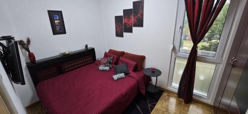 a bedroom with a red bed with pillows and a window at Lux Apartman Stojanović in Belgrade