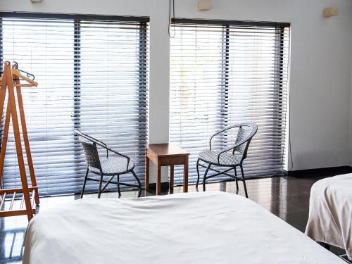 a bedroom with two chairs and a bed and windows at Calm Lanai Harbor in Nichinan