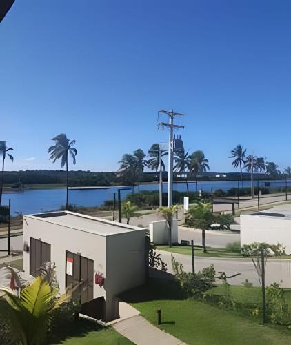 a building with palm trees and a body of water at Apartamento Pé na Areia Cond Alphaville Guarajuba in Camaçari