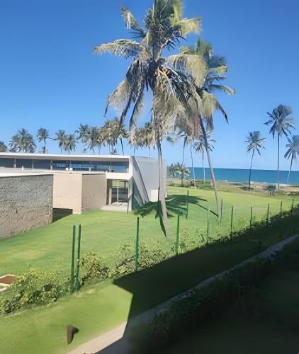 a building with palm trees in front of the ocean at Apartamento Pé na Areia Cond Alphaville Guarajuba in Camaçari