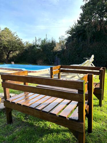 a wooden bench sitting in the grass next to a pool at Mini cabaña El Solcito, tranquilidad a dos cuadras de la Laguna de Chascomús in Chascomús