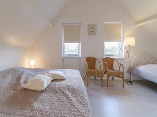 a bedroom with a bed and two chairs and two windows at Cozy Zeeland Retreat with a Sauna in Wemeldinge
