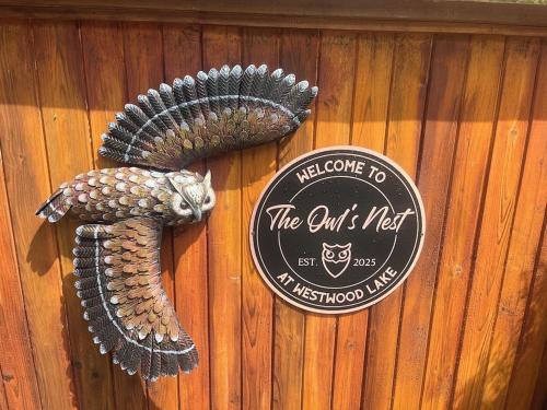 a sign on a wooden wall with a bird statue at The Owls Nest at Westwood Lake in Nanaimo
