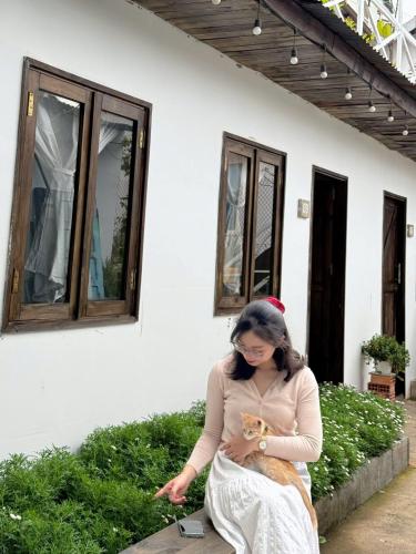 a woman sitting in front of a house holding a cat at Nằm Mơ 2 Homestay - chi Nhánh Ngô Quyền in Da Lat