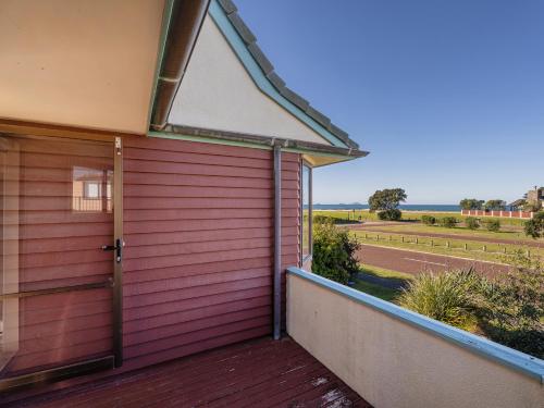 a red house with a door and a balcony at Beachfront Landing - Pauanui Holiday Home in Pauanui