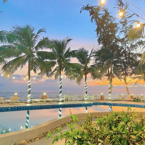 a resort swimming pool with palm trees and the ocean at Resort HAVANA in Mui Ne