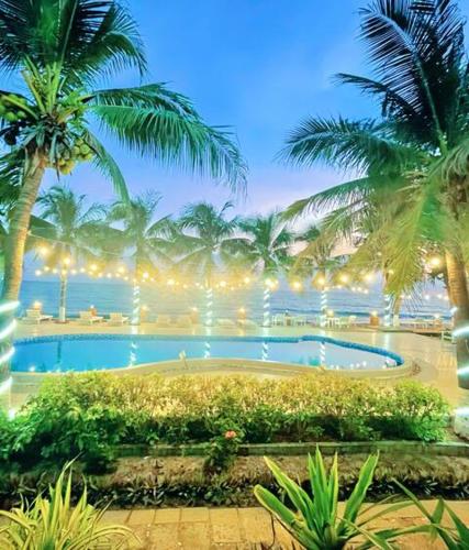 a large swimming pool with palm trees and the ocean at Resort HAVANA in Mui Ne