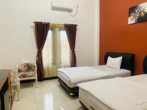 a room with two beds and a chair and a window at Hotel Nascar Famili in Palangkaraya