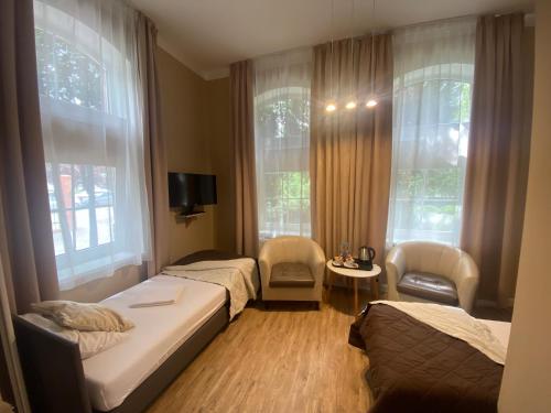 a bedroom with two beds and two chairs and windows at Hotel Kamil in Kwidzyn