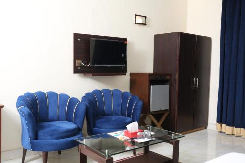 a living room with blue chairs and a table and a tv at Royalton Inn Hotel - Liberty in Lahore