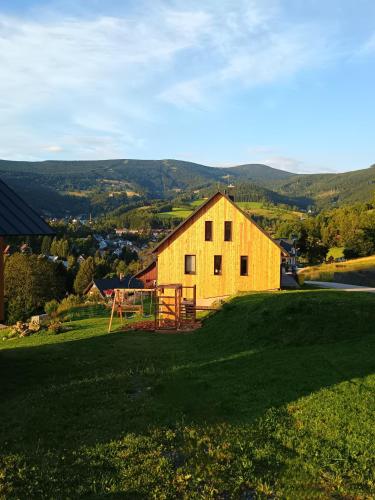 a yellow barn on a hill with a green field at Výhledovka chalet in Rokytnice nad Jizerou