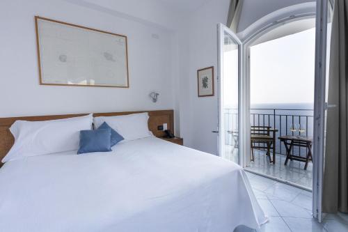 a bedroom with a white bed and a balcony at Hotel Punta Scario in Malfa