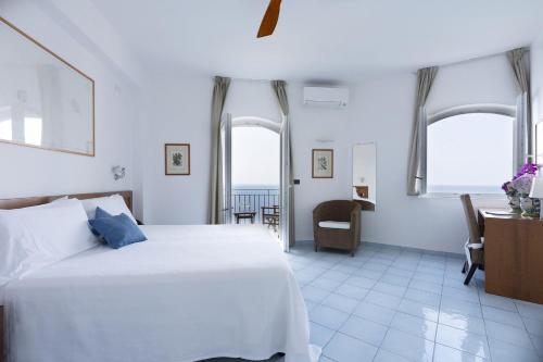 a bedroom with a bed and a desk and windows at Hotel Punta Scario in Malfa