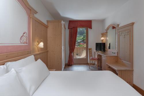 a bedroom with a white bed and a desk at Beverly Alps Hotel & Spa in Pinzolo