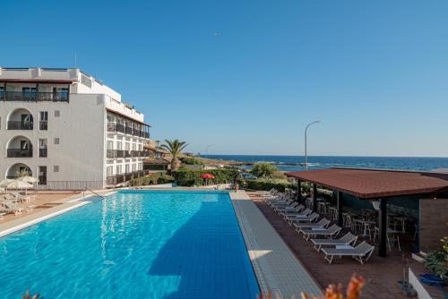 a swimming pool with chairs and a building and the ocean at Hotel Calabona in Alghero