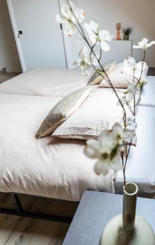 a bed with pillows and a vase with flowers on a table at Newly Built Nature Villa, Wifi And Clean in Ledeacker