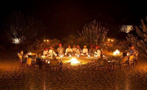 a group of people sitting around a fire pit at night at Morocco Luxury Camp Sam in Sām