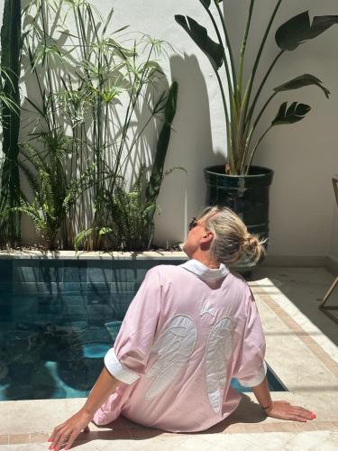 a woman sitting on the floor next to a swimming pool at Riad Reflet D'orient Marrakech in Marrakech