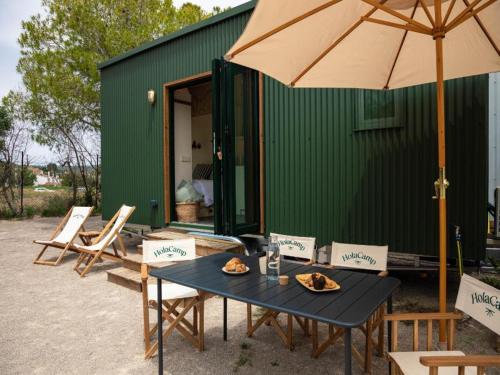 a table with chairs and an umbrella in front of a green building at HolaCamp Sitges Garrofer in Sitges
