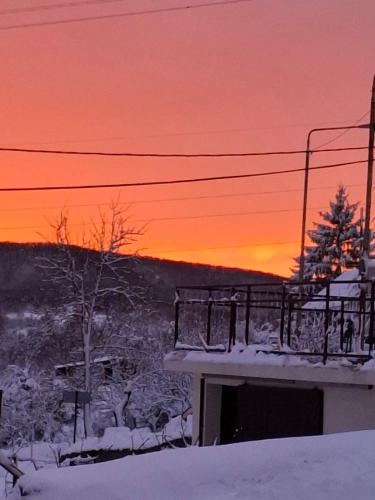 a sunset over a building with snow and a tree at Brkinka Apartments in Vremski Britof