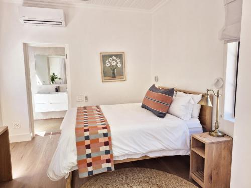 a white bedroom with a bed and a mirror at Minserie Collection in Stellenbosch