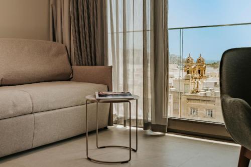 a living room with a couch and a table in front of a window at Regional Hotel by NEU Collective in Il-Gżira