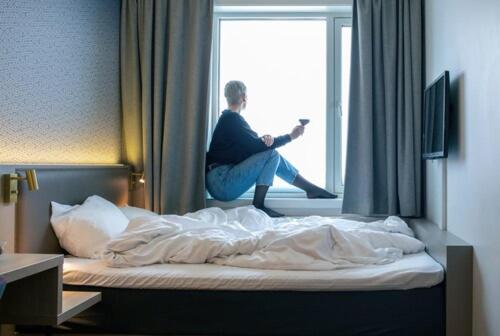a man sitting on a bed looking out the window at Comfort Hotel Xpress Tromsø in Tromsø